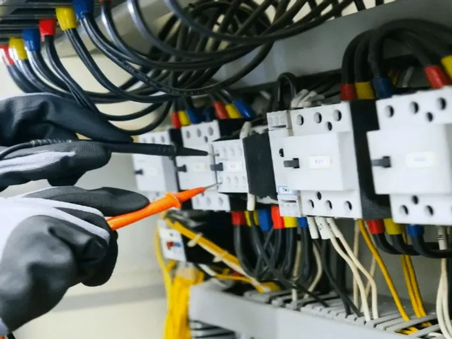 Electrician's gloved hands testing wiring in an electrical control panel